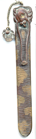  This bookmark was made in Japan. It is made of copper and brass and has an octopus on top. Two of the optopus' tentacles are outstretched and have captured it's next meal which forms the top blade. Attached to the top by a chain is a flower. The date is 1900 - 1910.  